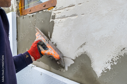 Construction worker covering house wall with adhesive cement glue berore installing styrofoam insulation sheets for thermal protection. photo