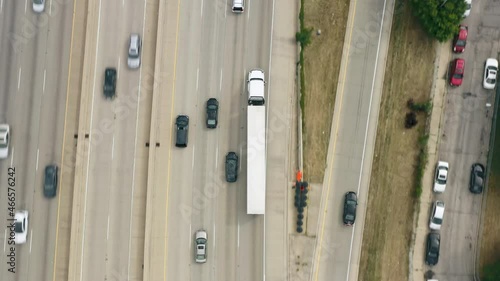 Semi Truck with white cargo trailer driving by busy highway road delivering goods. Highway top down view follow eco friendly truck vehicle aerial footage traffic. Emission free ecofriendly transport