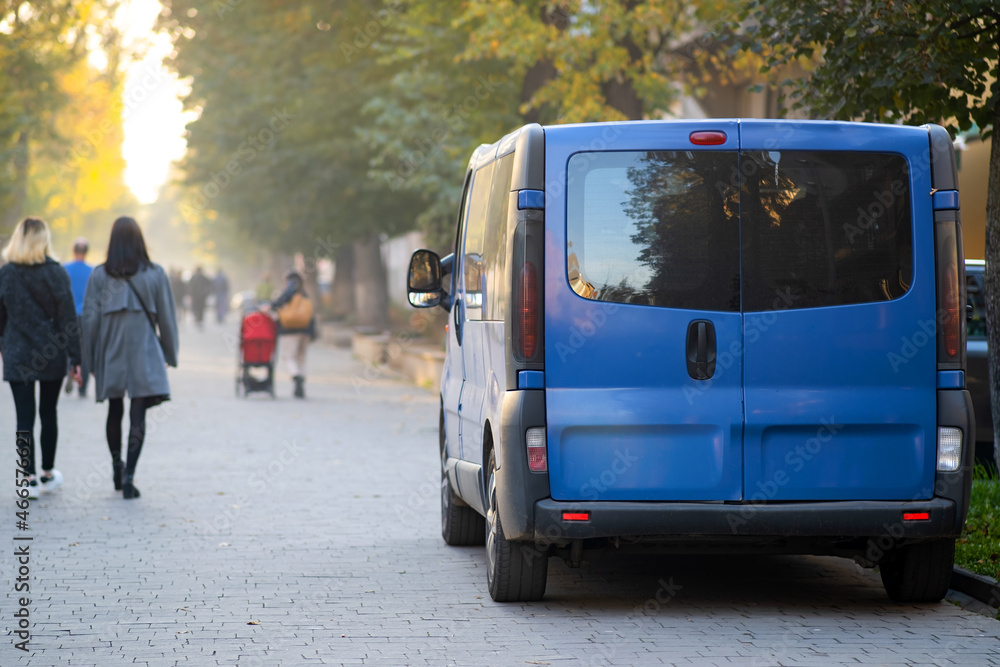 Φωτογραφία Passenger van car parked on a city alley street side with blurred walking pedestrians in autumn