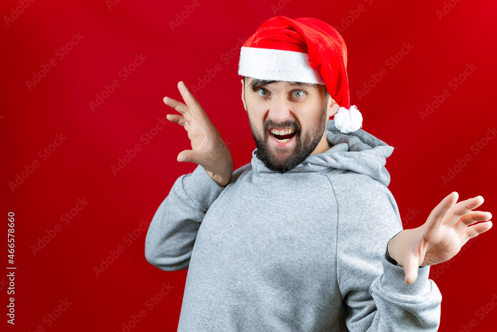 Fototapeta premium a bearded man in a red Santa Claus hat grins and makes various poses with his hands.
