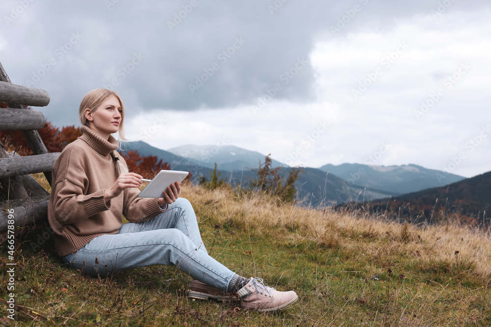 Young woman drawing on tablet in mountains, space for text