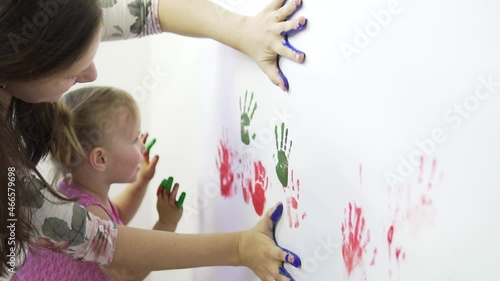 Mom and daughter make handprints using paints on white paper.Slow motion.