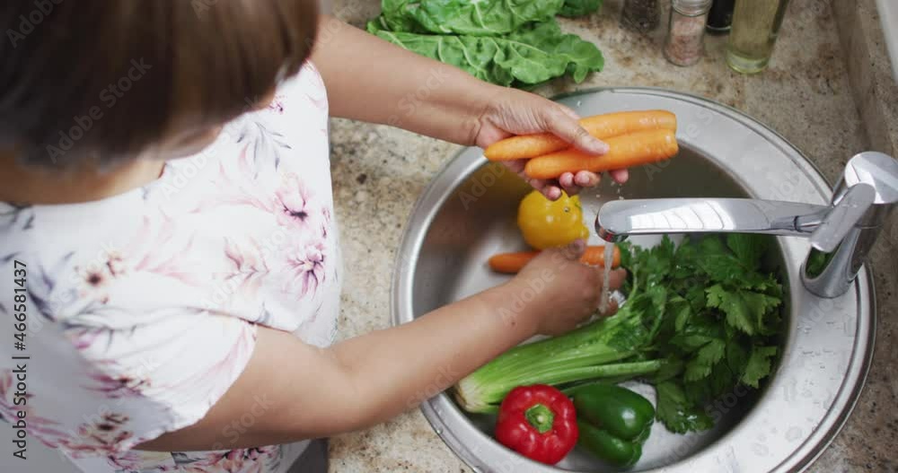 Overhead view of african american senior woman in kitchen washing vegetables under tap in sink Overhead view of african american senior woman in kitchen washing vegetables under tap in sink