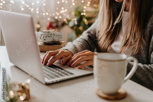 Close up of woman hands with, gifts, coffee cup and laptop. Online shopping at Christmas holidays. Freelance girl woking from home office. Female typing at notebook computer. Christmas moments.