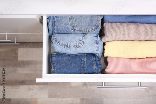 Open drawer with folded clothes indoors, top view. Vertical storage photo