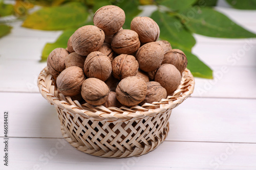 Wicker bowl of ripe walnuts on white wooden table