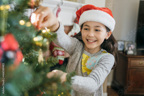 Happy girl in Santa had decorating Christmas tree with ornaments