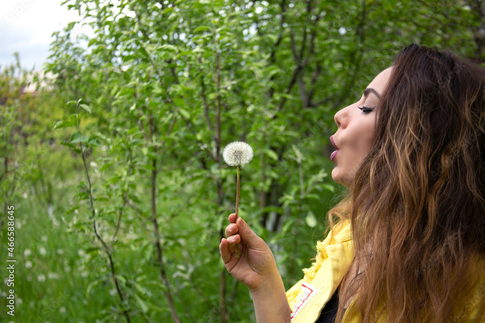 Beautiful young woman blowing dandelion while standing