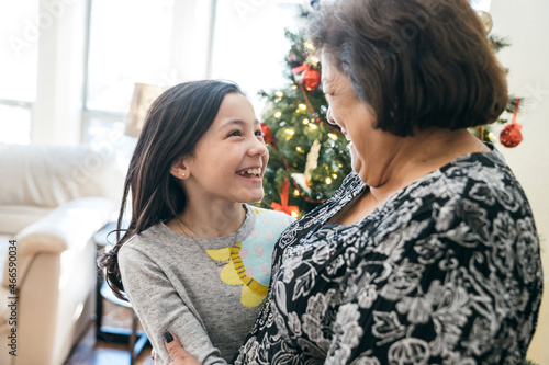 Girl looking at grandma and laughing in front of Christmas tree