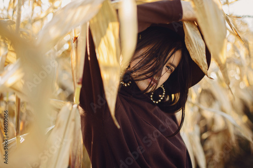 Wallpaper Mural Portrait of stylish woman in hat and brown clothes posing in autumn maize field in warm sunny light. Fashionable attractive young female  standing in autumnal corn in evening countryside Torontodigital.ca