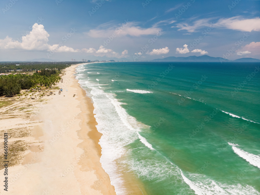 Aerial view of beautiful vietnamese landscape, beach by emerald South China Sea near Hoi An under blue cloudy sky, and distant city Da Nang, Vietnam