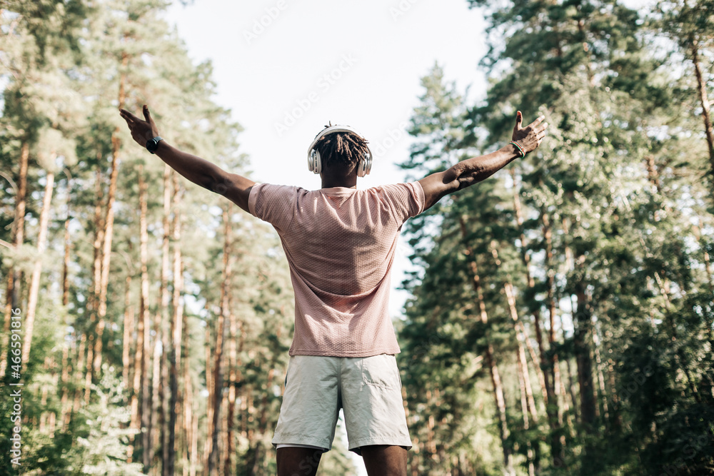 African American fitness man, wearing headphones, standing on the road with raised arms, enjoying freedom,