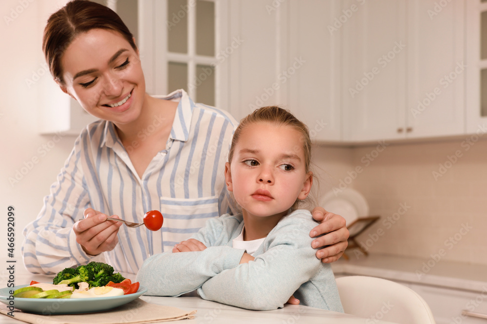 Mother feeding her daughter in kitchen. Little girl refusing to eat dinner Mother feeding her daughter in kitchen. Little girl refusing to eat dinner