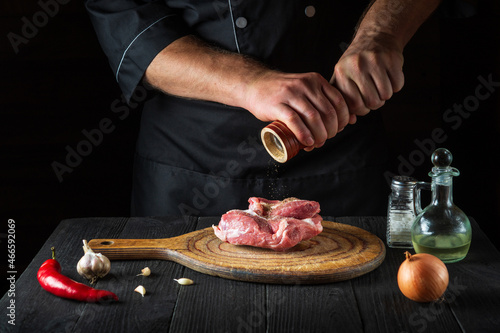 Chef cooking raw meat fillet and adding pepper or chili for marinade. Working environment in kitchen in restaurant or cafe.