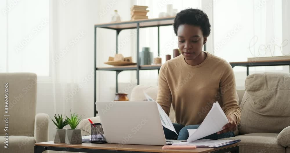 Woman writing notes while analyzing documents and working on laptop at home Woman writing notes while analyzing documents and working on laptop at home