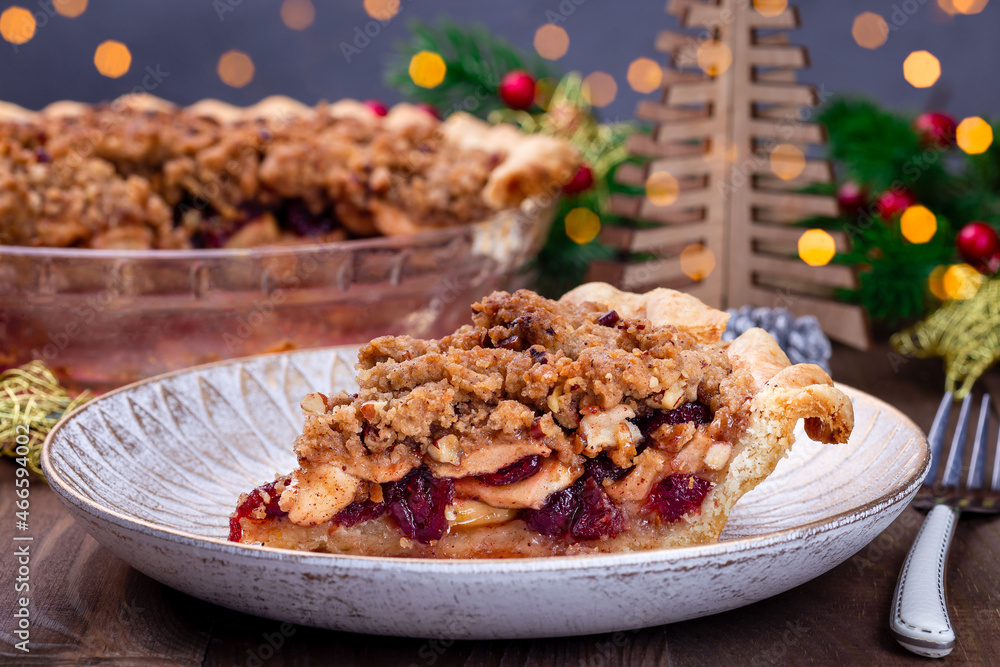 Fototapeta premium Slice of American apple cranberry pie, topped with crumbled dough and pecan, bokeh on background