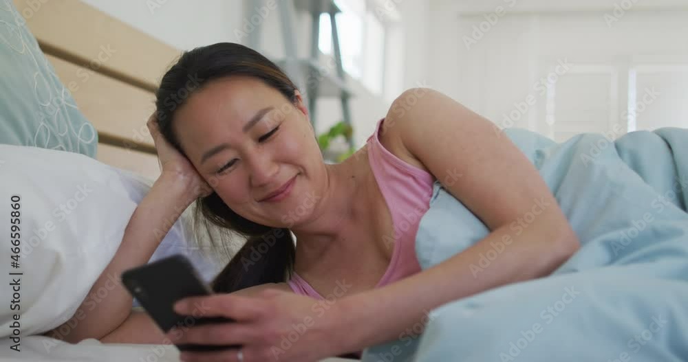 Happy asian woman lying in bed, using smartphone in the morning Happy asian woman lying in bed, using smartphone in the morning