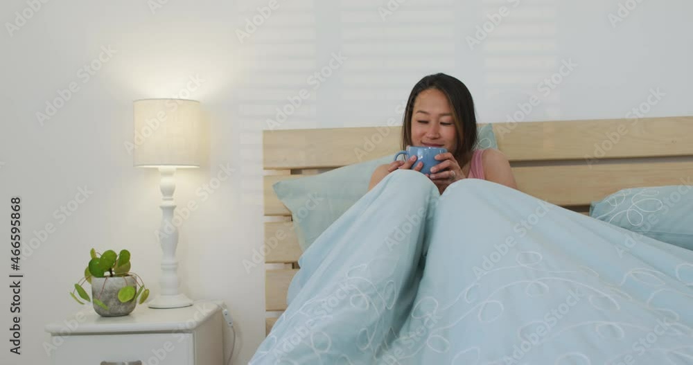 Happy asian woman lying in bed, drinking coffee in the morning Happy asian woman lying in bed, drinking coffee in the morning
