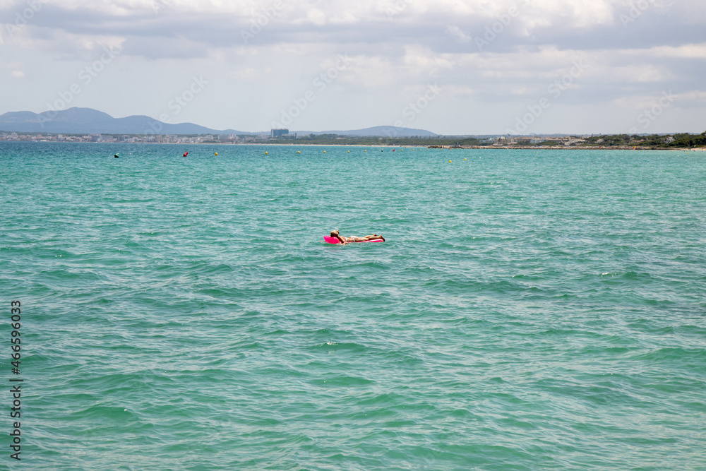 A middle aged man swimming and laying down on a pool inflatable lilo in the ocean off the coast of Majorca in Spain