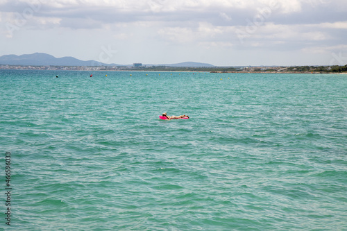 A middle aged man swimming and laying down on a pool inflatable lilo in the ocean off the coast of Majorca in Spain