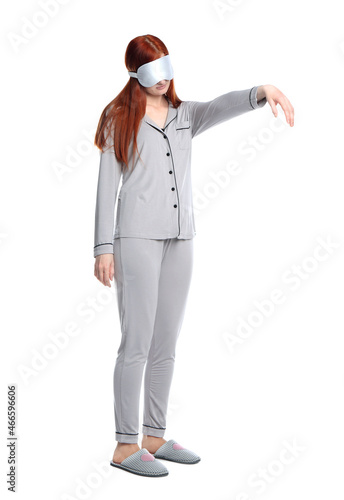 Young woman wearing pajamas, mask and slippers in sleepwalking state on white background