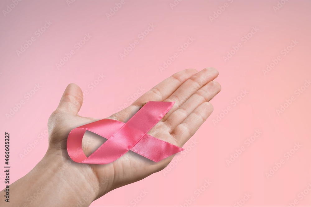 Persons hand holding the pink ribbon in palm symbol of breast cancer awareness Persons hand holding the pink ribbon in palm symbol of breast cancer awareness