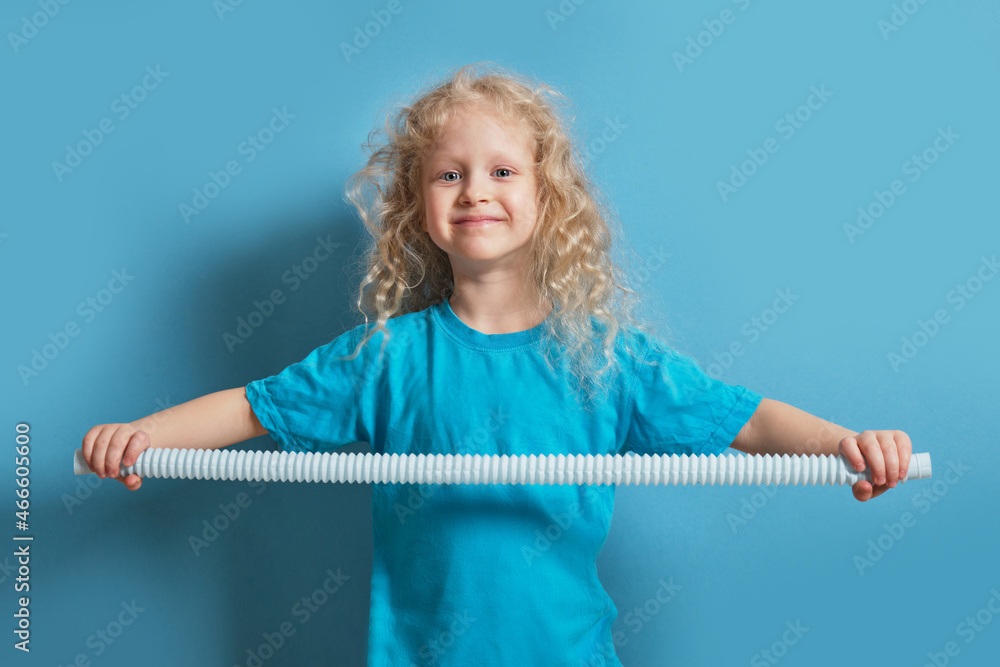 cute caucasian girl with curly blonde hair playing with pop it tube toy on blue background cute caucasian girl with curly blonde hair playing with pop it tube toy on blue background
