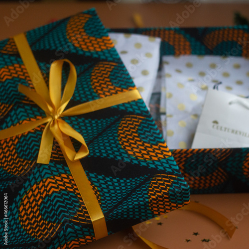 Christmas gift box wrapped in green print and golden bow surrounded with holly and fir against a brown background