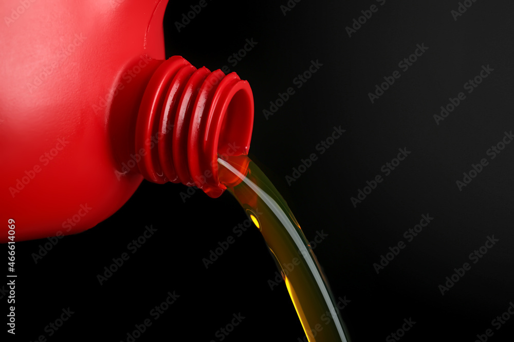 Pouring of motor oil from canister against black background, closeup Pouring of motor oil from canister against black background, closeup