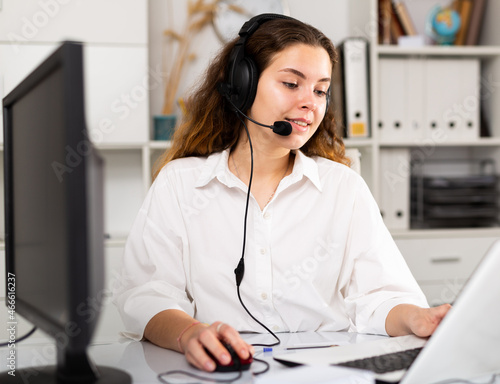Young positive woman customer support phone operator in microphone headset working on laptop in the office