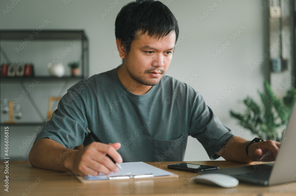 Asian business man thinking while serious working on laptop sitting on desk in modern office at home ,co-working space or at home with copy space, webinar over the internet. Asian business man thinking while serious working on laptop sitting on desk in modern office at home ,co-working space or at home with copy space, webinar over the internet.
