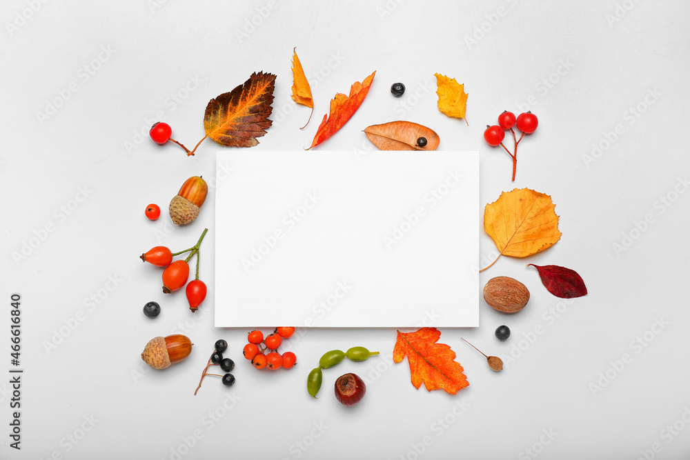 Fototapeta premium Autumn harvest frame with blank white card, seasonal fall leaves, berries, and nuts on a light background