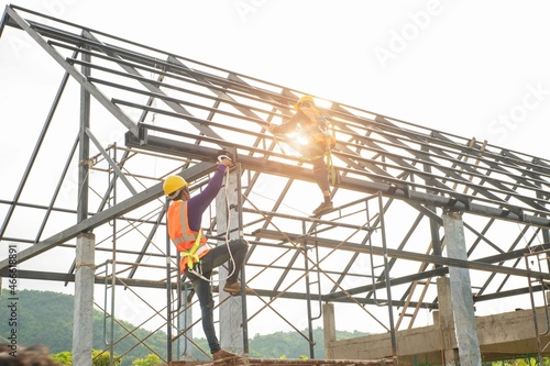 A construction teamwork in the construction of metall roof structures on construction site and sunset background..action plant safety teamwork concept.