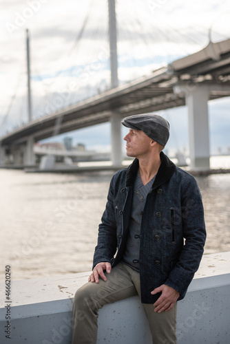 A man in a coat and a cap on the background of the bridge. © Artsiom P