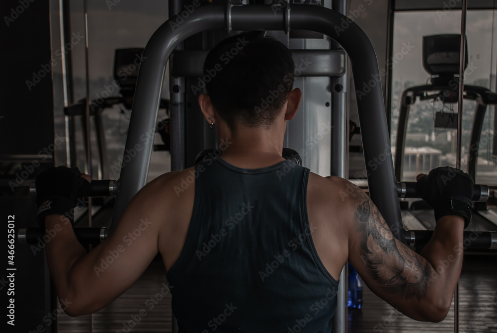 The back of bodybuilders exercise with lifting weights on an exercising machine in gym or fitness club. Selective focus. The back of bodybuilders exercise with lifting weights on an exercising machine in gym or fitness club. Selective focus.