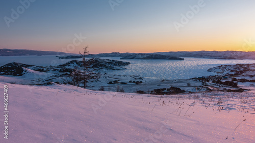 Dawn over the frozen Siberian lake. The sky is highlighted in orange. The glare of the sun on the ice. Sparkling snow in the foreground. The golden hour. Baikal © Вера 