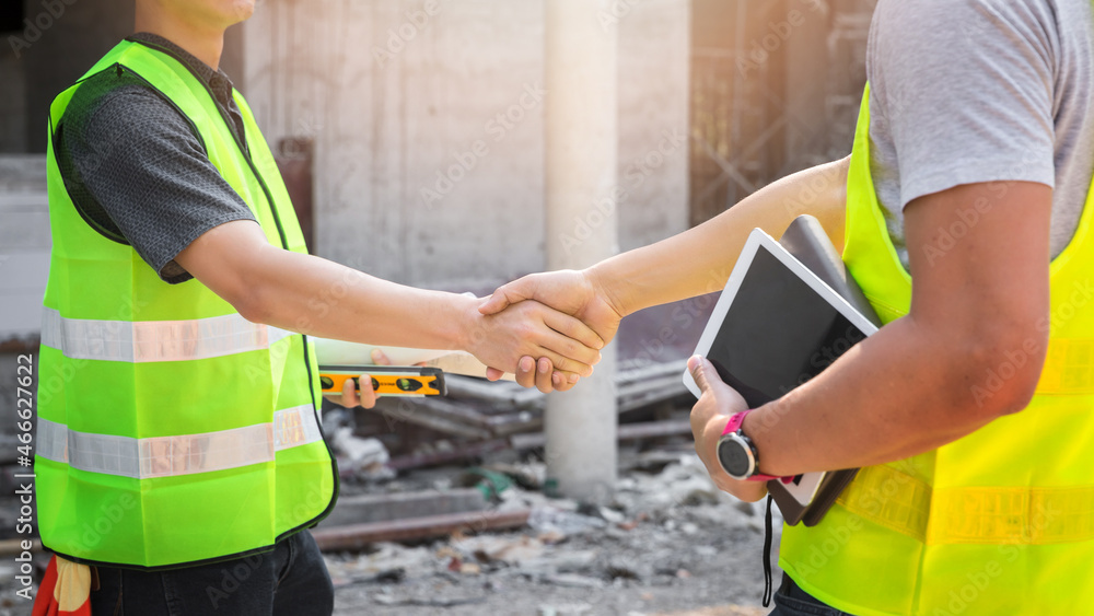 Teamwork, partnership, gesture concept. Builders greeting each other with handshake on construction site. construction workers in protective helmets and vests are shaking hands. Teamwork, partnership, gesture concept. Builders greeting each other with handshake on construction site. construction workers in protective helmets and vests are shaking hands.
