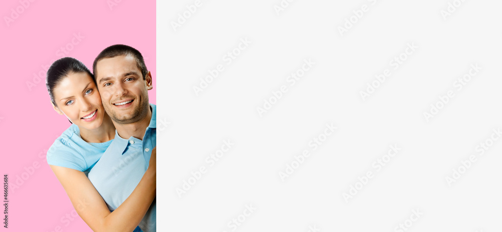 Portrait of happy smiling embracing attractive couple peeping from empty sign board billboard with copy space, isolated over rose pink colour background. Young man and woman at studio. Portrait of happy smiling embracing attractive couple peeping from empty sign board billboard with copy space, isolated over rose pink colour background. Young man and woman at studio.