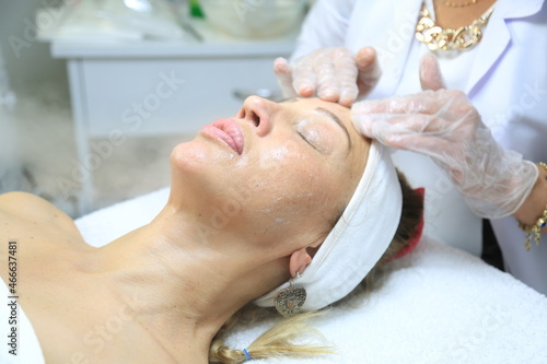 Facial peeling mask, spa beauty treatment, skin care. Woman getting facial treatment by beauty at spa salon, side view close up. Beautiful woman getting face massage in beauty spa