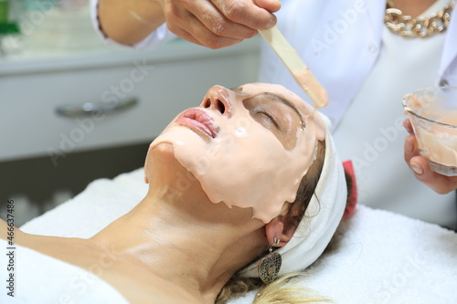Facial peeling mask, spa beauty treatment, skin care. Woman getting facial treatment by beauty at spa salon, side view close up. Beautiful woman getting face massage in beauty spa