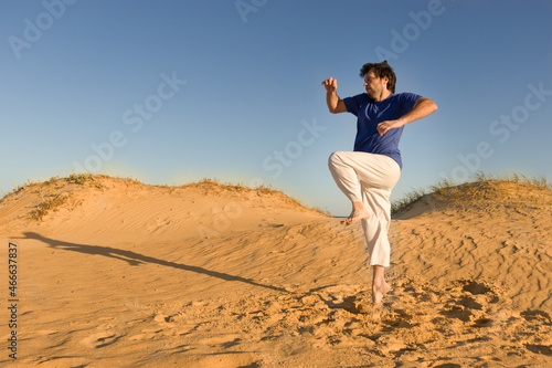 joven practicando artes marciales al atardecer sobre dunas de arena, saltando 