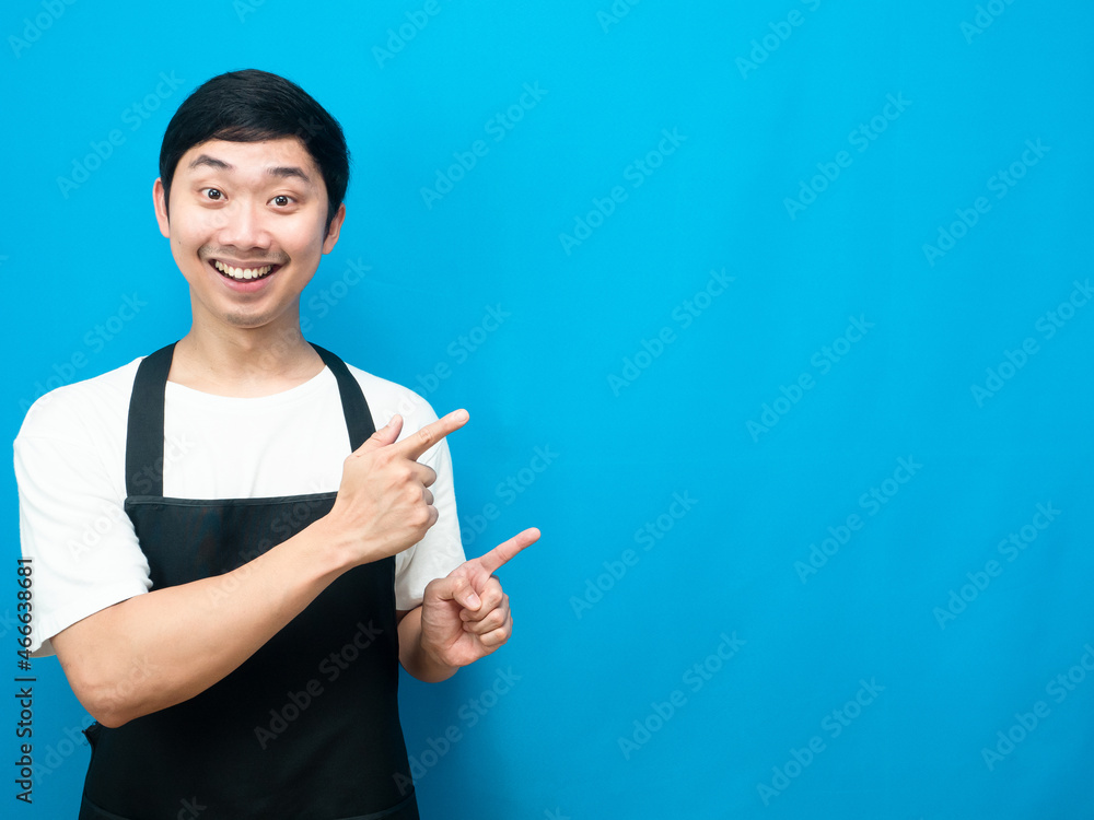 Asian man wearing apron happy smile point finger at copy space blue background Asian man wearing apron happy smile point finger at copy space blue background