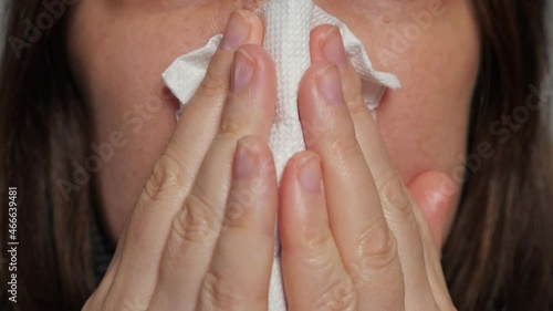 Brunette woman wearing warm sweater catches cold and suffers from runny and stuffy nose snotting into paper napkin extreme closeup.