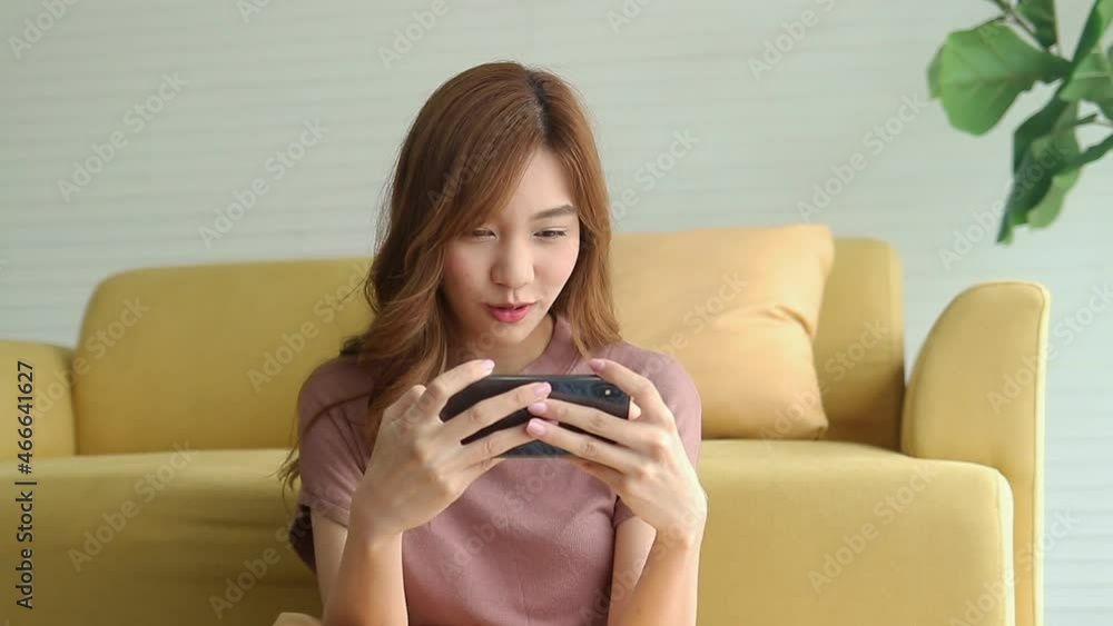 Beautiful Asian woman relaxing in an apartment She is having fun playing online games on her smartphone. concept of using modern communication technology Beautiful Asian woman relaxing in an apartment She is having fun playing online games on her smartphone. concept of using modern communication technology