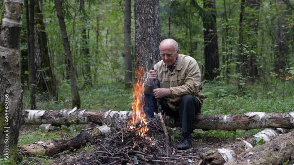 A lonely old tourist is warming himself by a campfire in the forest. He was very cold on an autumn hike. A lonely old tourist is warming himself by a campfire in the forest. He was very cold on an autumn hike.