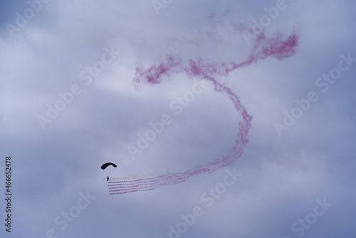 Parachutist with red smoke at Axalp Canton Bern air show of Swiss Air Force on a cloudy grey autumn day. Photo taken October 19th, 2021, Brienz, Switzerland.
