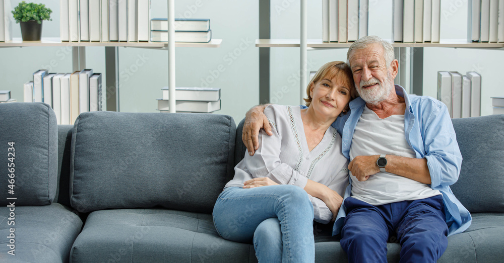 Caucasian old senior romantic aged lover couple in casual wear gray bearded and hair grandpa husband and lovely grandma wife sitting smiling cuddling hugging together on sofa