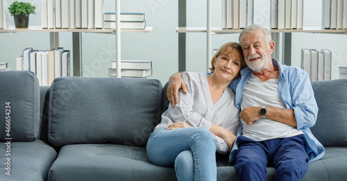 Caucasian old senior romantic aged lover couple in casual wear gray bearded and hair grandpa husband and lovely grandma wife sitting smiling cuddling hugging together on sofa