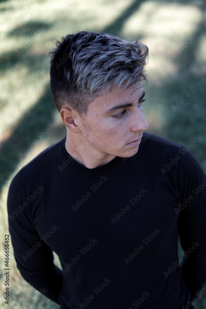 Young teenager with light-colored hair, wearing a black shirt leans against a square tiled wall Young teenager with light-colored hair, wearing a black shirt leans against a square tiled wall