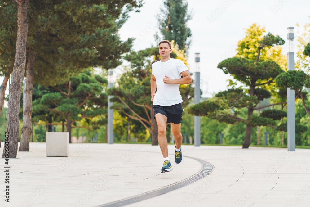 Attractive young man athlete wearing sportswear run in modern park at summer morning